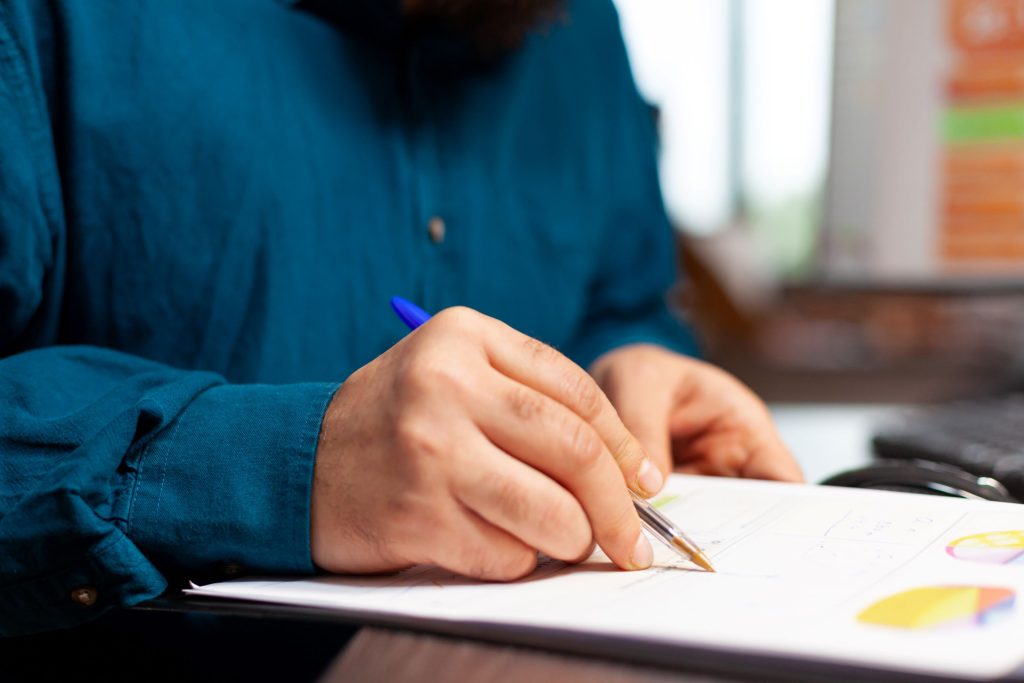 Person reviewing charts and writing notes on a report at a desk.
