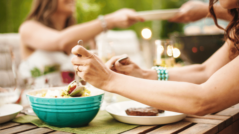 Adults sharing food at an outdoor table, representing social eating and mealtime participation.