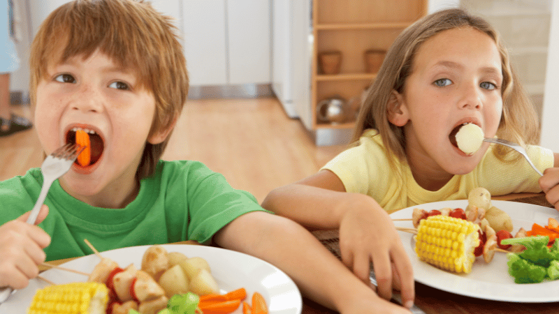 Two children sitting at a table sharing a calm mealtime with simple foods.