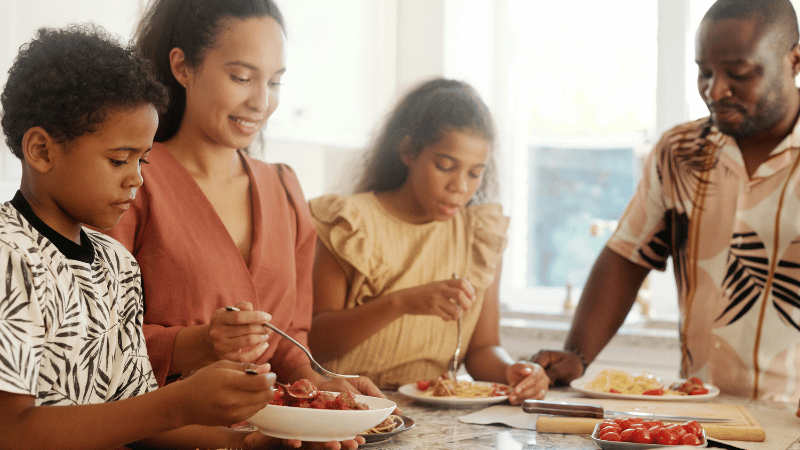 Group of people sharing a meal at a dining table, representing mealtime participation and social eating for children and teens.