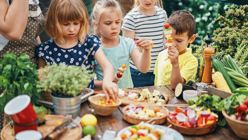 Children preparing vegetable skewers outdoors, representing sensory food exploration and positive, low‑pressure feeding experiences.