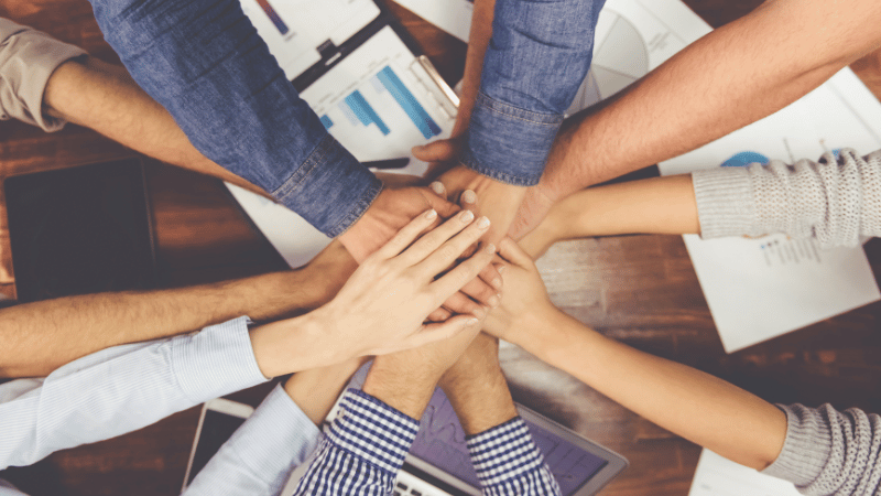 Hands stacked together in a collaborative gesture, representing multidisciplinary teamwork.