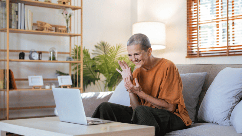 Person sitting on a sofa using a laptop for a telehealth session, representing remote feeding support for NDIS participants.