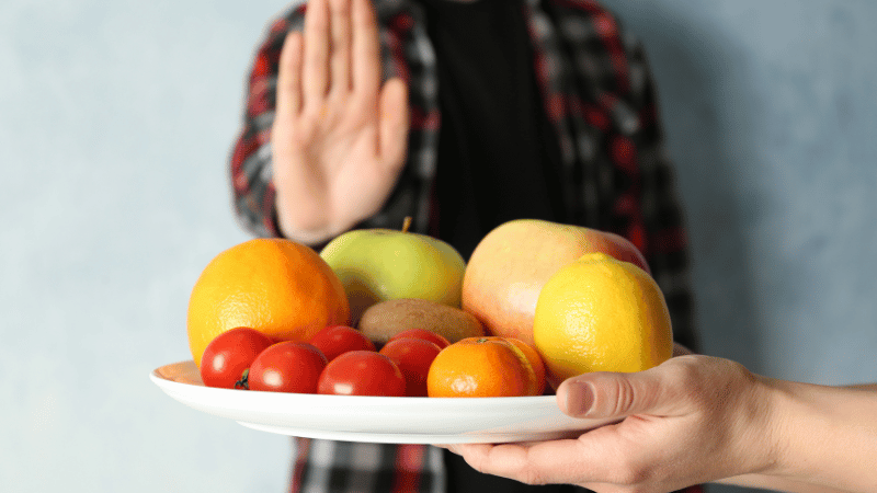 Person raising a hand to decline an offered plate of food, representing service boundaries and supports not offered under NDIS.