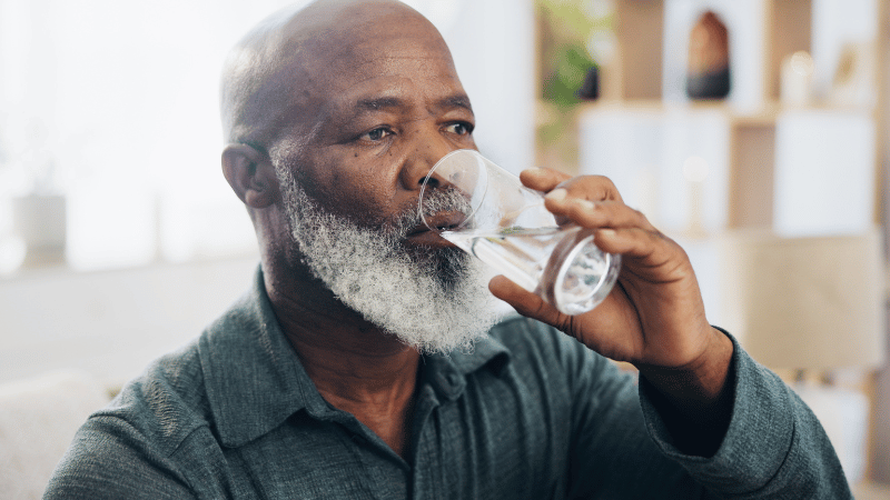 Older adult drinking water indoors, representing hydration and everyday mealtime routines.