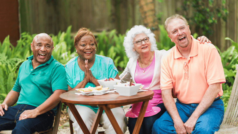 Older adults sitting together at an outdoor table, sharing food and enjoying a relaxed social mealtime.
