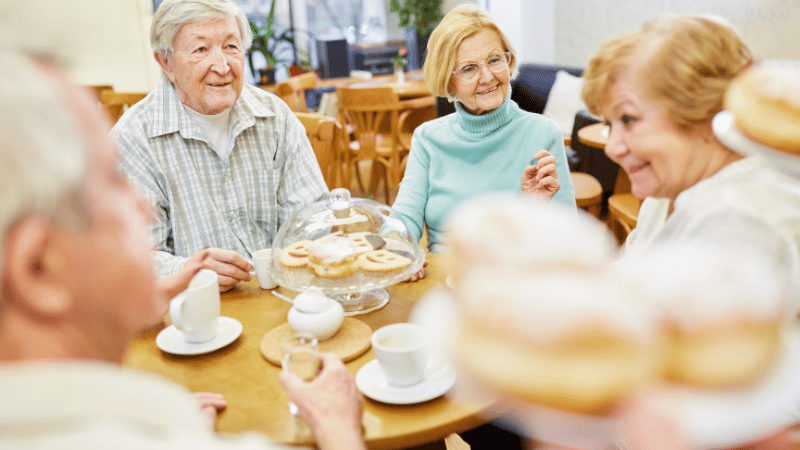 Older adults sitting together at a café table, enjoying drinks and pastries, representing social eating and community participation.