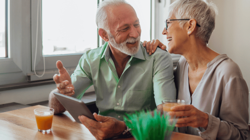 Two older adults sitting at a table using a tablet, representing telehealth feeding support.