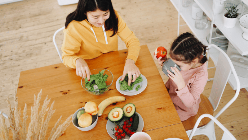 Parent and child sitting at a table exploring fresh foods together during a calm mealtime.