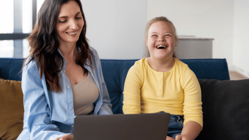 Adult and child sitting together with a laptop, representing parent coaching, guidance and supportive feeding strategies.