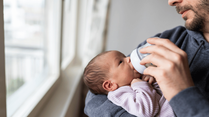 Adult holding and bottle‑feeding a newborn in a calm, responsive way, representing early signs a baby may benefit from feeding support.
