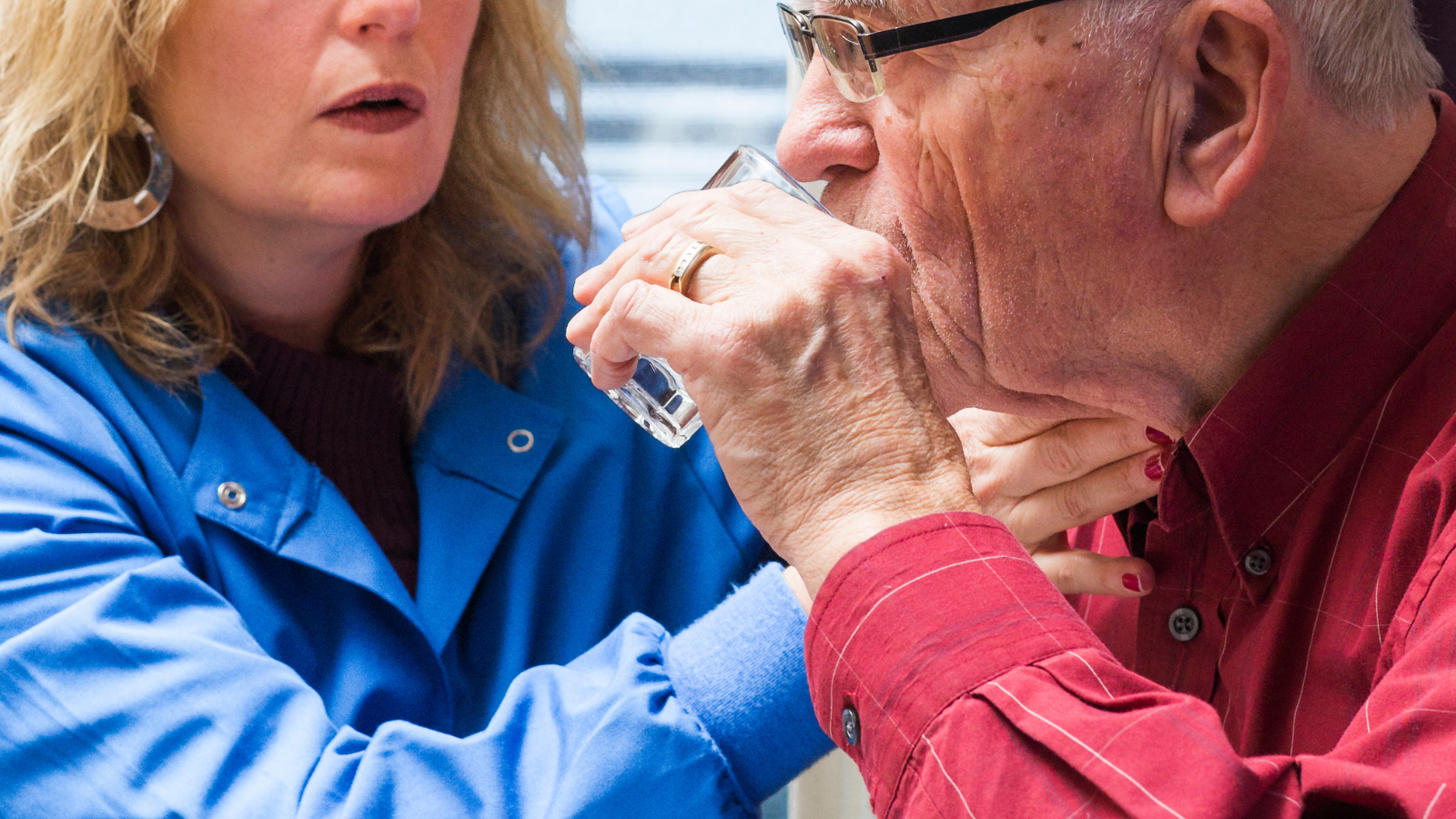 Clinician supporting an older adult during safe drinking, demonstrating hands‑on assistance used in swallowing (dysphagia) assessments.