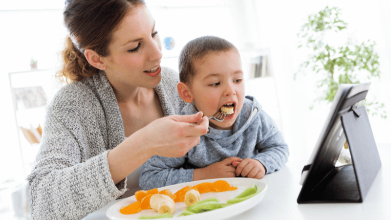 Parent supporting a child with eating during a video call, representing telehealth feeding assessment and therapy.