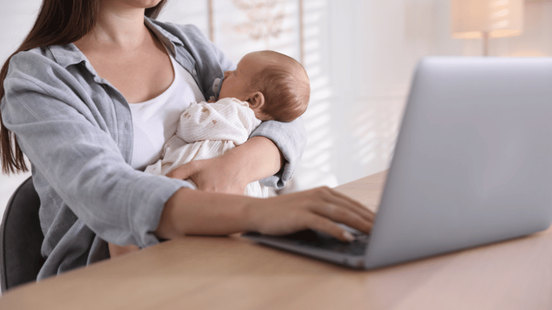 Parent holding a baby while using a laptop, representing telehealth options for infant feeding support.