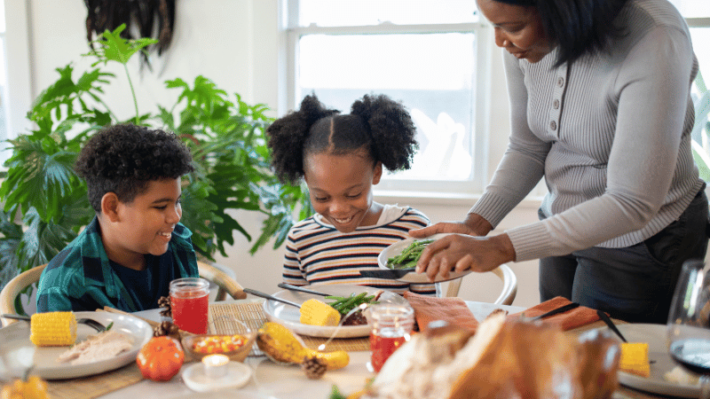 Parent serving vegetables onto a child’s plate during a calm mealtime, representing paediatric feeding support and family mealtime routines.