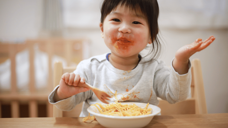 Toddler exploring spaghetti during a messy mealtime, representing sensory feeding experiences and early oral‑motor development.