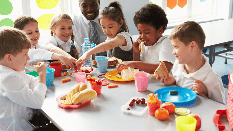 Children and a teacher at a table, representing educators, support workers and care teams who receive mealtime training.