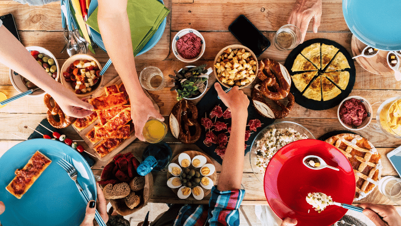 A colourful shared meal with a variety of foods on a table, showing different textures and mealtime interactions, used to represent feeding, mealtime routines and food diversity.